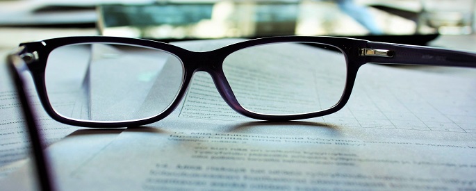 A pair of glasses sits atop various forms and papers