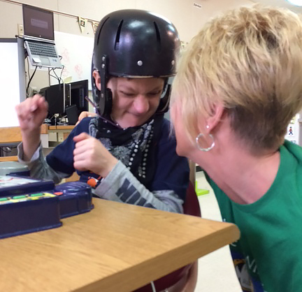A boy in a classroom who is wearing a helmet interacts positively with his intervener.