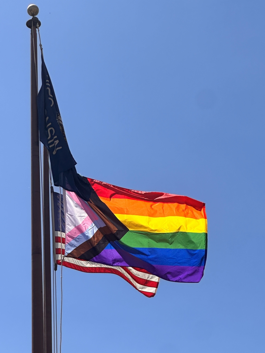 Pride flag flying in between the Wisconsin flag and the United States flag on the flagpole in front of the DPI offices