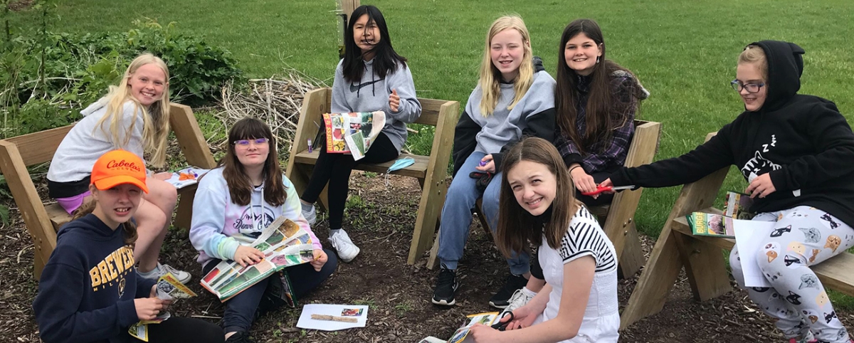 Group of middle school girls sitting on benches in a garden looking at seed catalogs