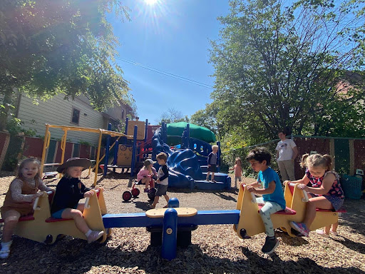Adorable three year olds sit atop a yellow teeter totter in the small outdoor space at the Creative Learning Preschool.