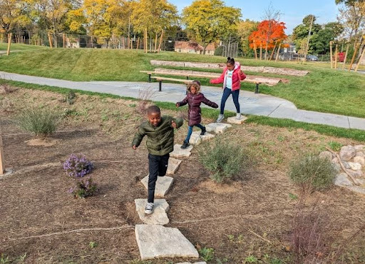 Three students at Hawthorne Elementary School in Milwaukee run along a newly-created stepping stone path surrounded by grasses. 
