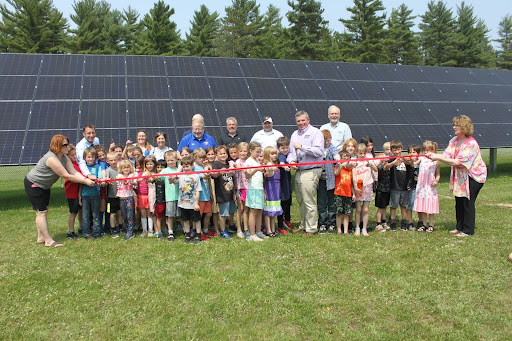 A large group of students stands in front of an impressive array of solar panels at a ribbon cutting ceremony.