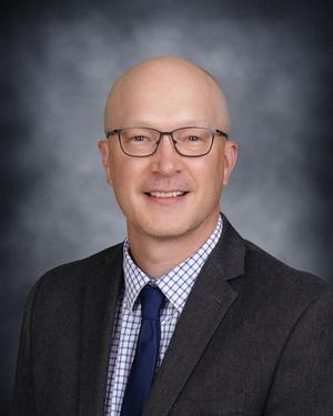 Josh Robinson, a smiling, bald, white man wearing a suit and tie