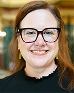 Dr. Barb Novak, a smiling white woman with long red hair and black rimmed glasses