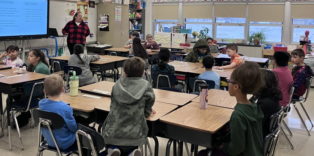 Teacher Mrs. Lambrecht from Lowell International Elementary School in Milwaukee Public Schools stands in front of a classroom of children on a Saturday morning in December 2023. The students are chatting and engaged with one another.