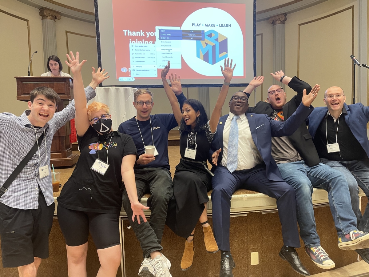 Chris Baker, Dr. Williams, day two's keynote speaker Dr. Rilla Khaled, and some attendees taking a fun picture onstage before the morning's breakout sessions. Participants are standing in front of a screen where the powerpoint presentation is being projected, and they're making goofy poses, smiling, and doing jazz hands. 