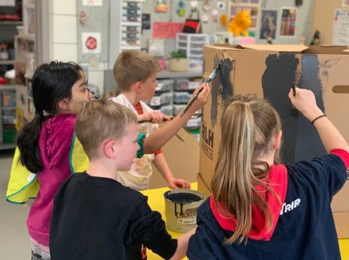 Children painting a large cardboard box