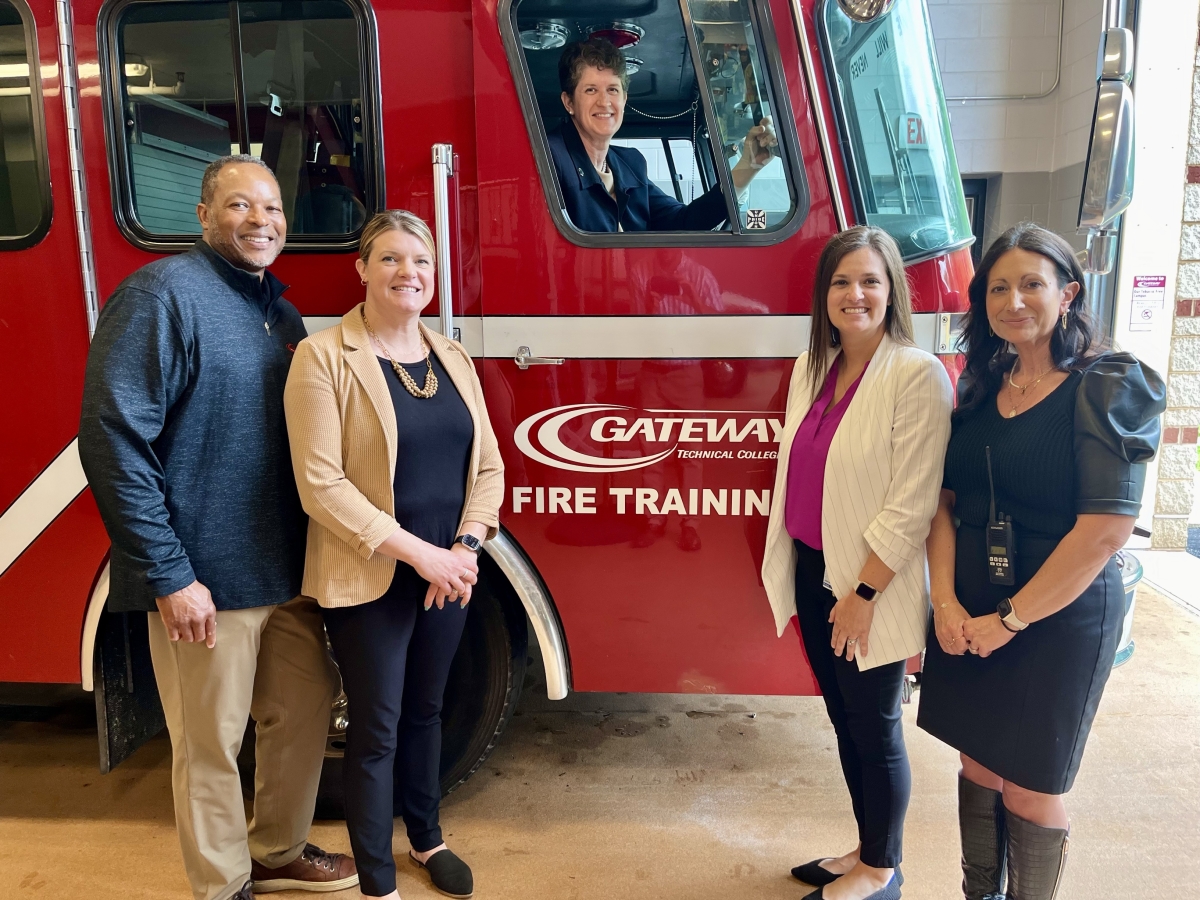 Dr. Jill Underly poses with educators at Burlington High school. She is smiling and behind the wheel of a fire truck used in their Career and Tech Ed program, while the educators pose around her. 
