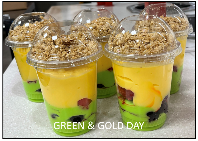 Five colorful yogurt and fruit parfaits with a layer of green-colored yogurt below a layer of gold-colored yogurt 